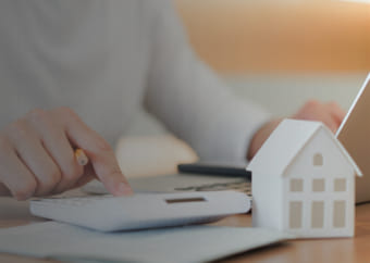 Realtor using a calculator at a desk with a tiny model of a house