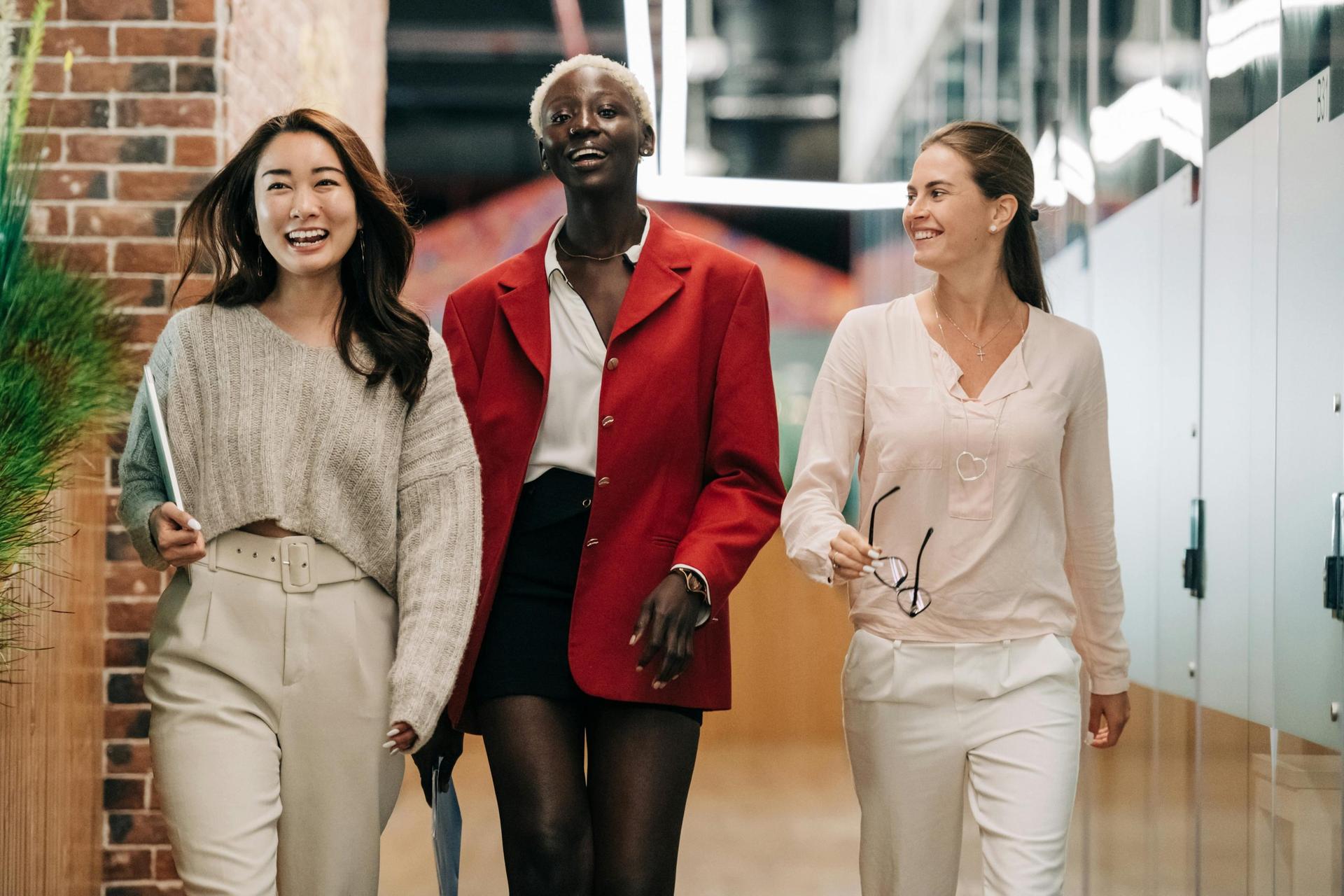 Three professional women walking confidently across an office hallway.